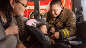 photo: fireman helping Native American mother with her child's car seat.